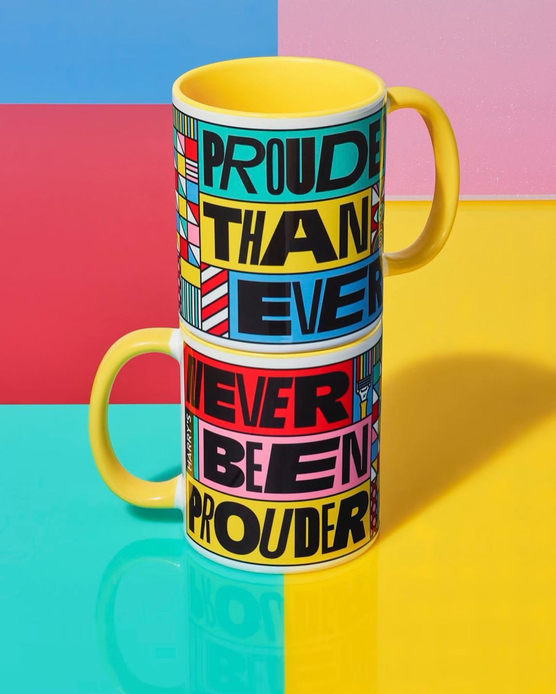 Two yellow mugs stacked with colorful graphic design and the text, 'Prouder Than Ever' and 'Never Been Prouder' against a split color background.