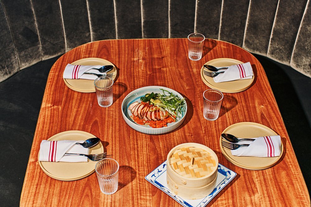 Overhead view of a wooden table in a restaurant setting, laid out with plates, cutlery, napkins, water glasses, and a central food dish.