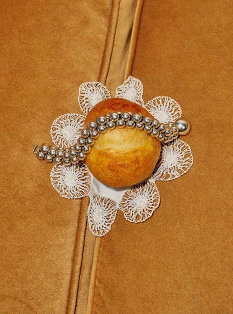 Overhead shot of an apple on a white lace doily, adorned with a silver beaded bracelet, set against a brown fabric background.
