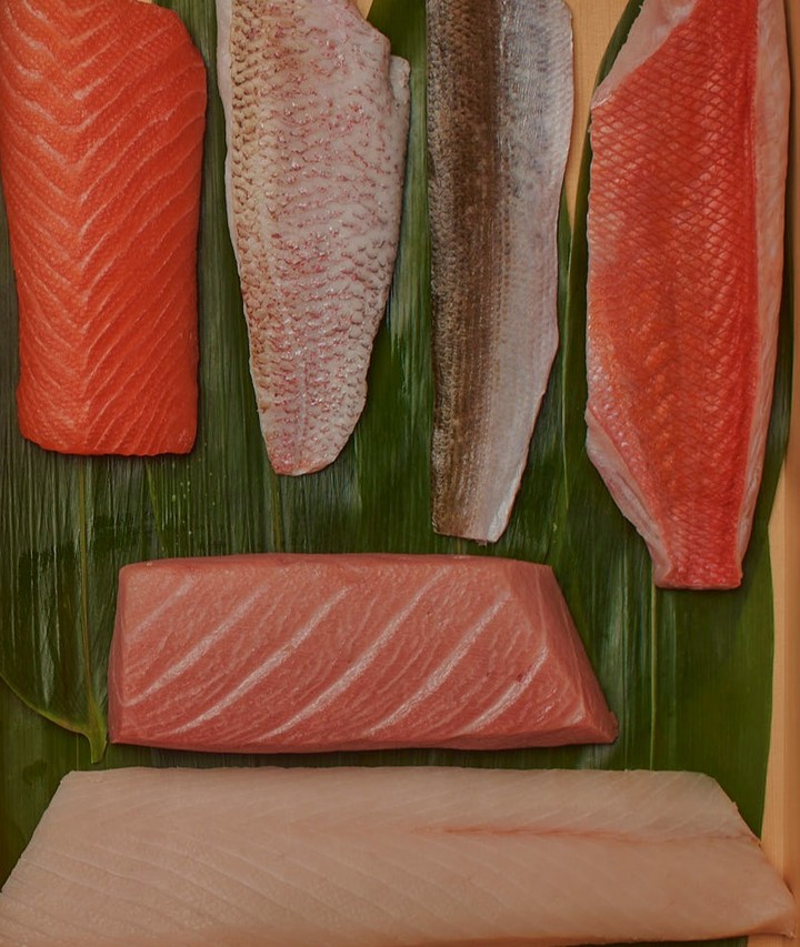Assortment of fresh fish fillets, including salmon and tuna, artfully arranged on green leaves, showcasing vibrant colors and textures.