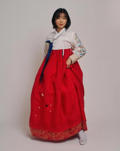 Full-length studio shot of a young Asian woman in a traditional Korean hanbok dress with bright red skirt and white top with embroidery.