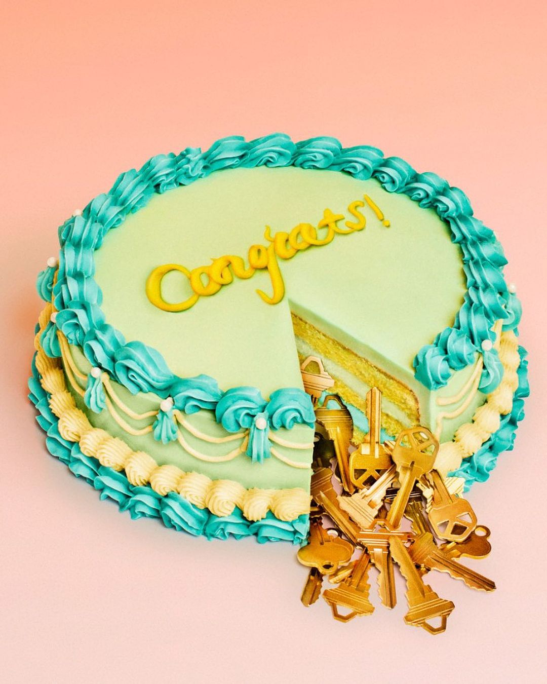 Celebratory cake with golden 'Congrats!' inscription, a slice removed revealing golden keys spilling out, set against a pink backdrop.