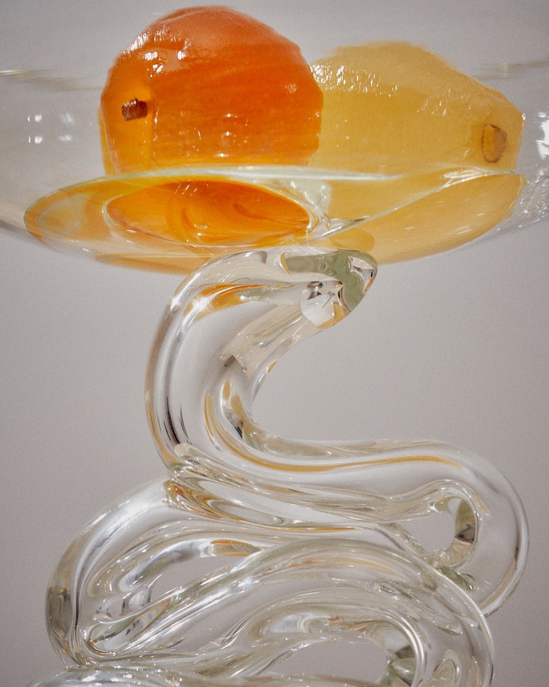 A glass sculpture with an orange fruit and yellow gelatin on top, displaying a modern art composition with clear and bright lighting.