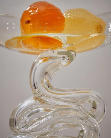 A glass sculpture with an orange fruit and yellow gelatin on top, displaying a modern art composition with clear and bright lighting.