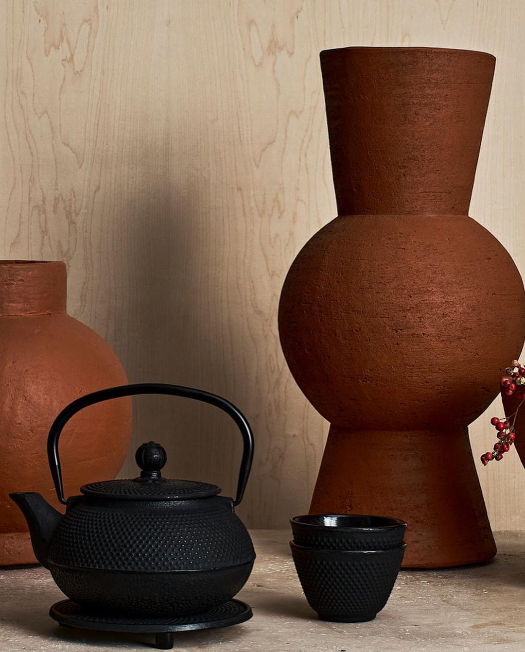Still life with a black teapot, teacup, and red-brown ceramic vases against a light wood background, creating a simple and elegant composition.