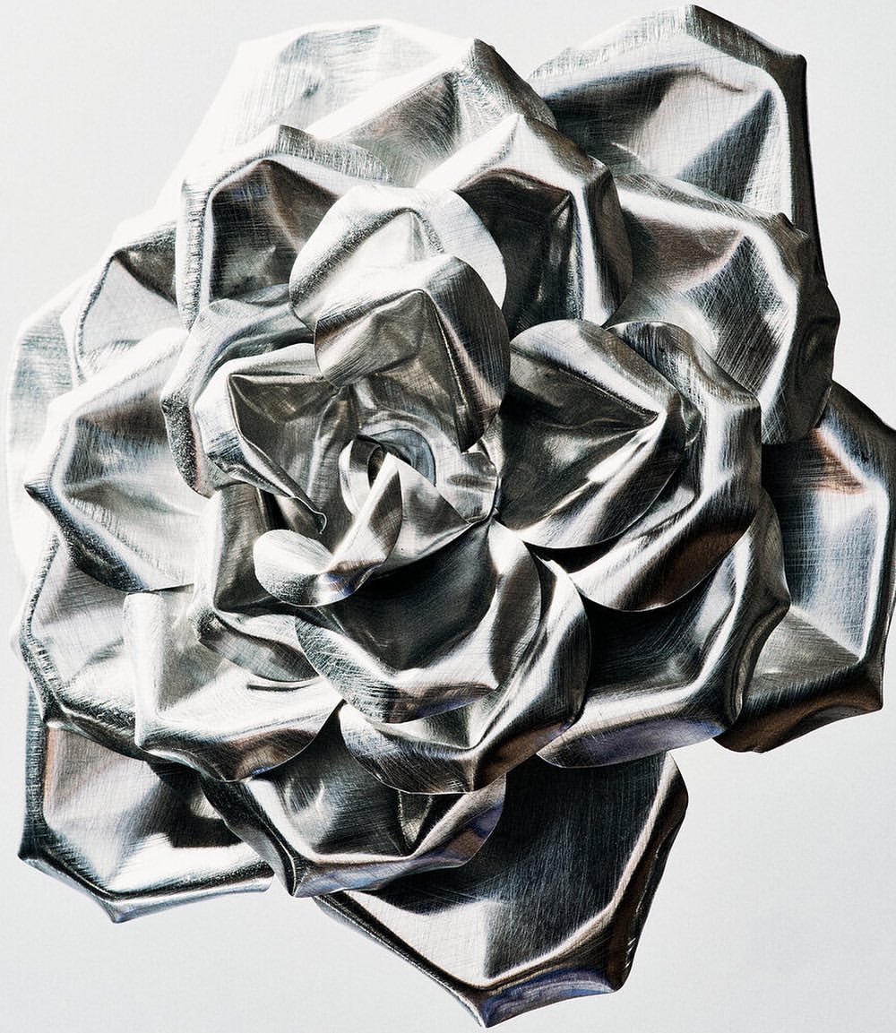 Macro shot of an abstract silver rose made from metallic foil, showcasing textures and light reflections against a white background.