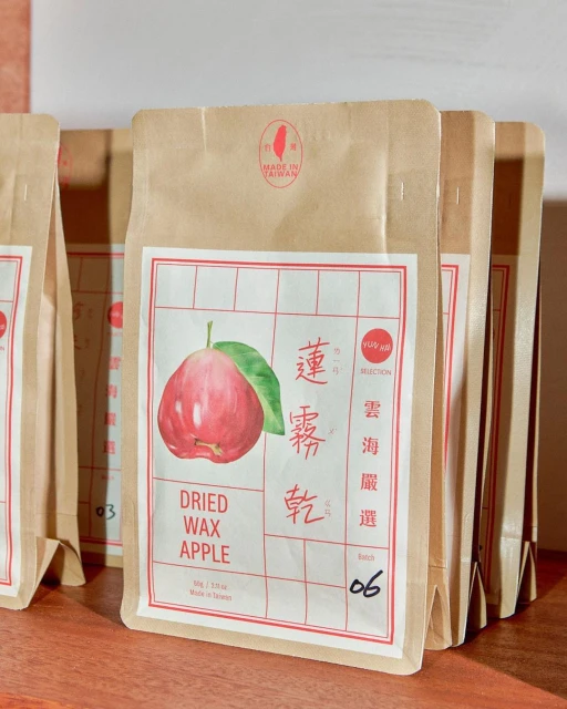 Close-up of multiple kraft paper bags filled with dried wax apple, each bag features a watercolor graphic of the fruit on the front.