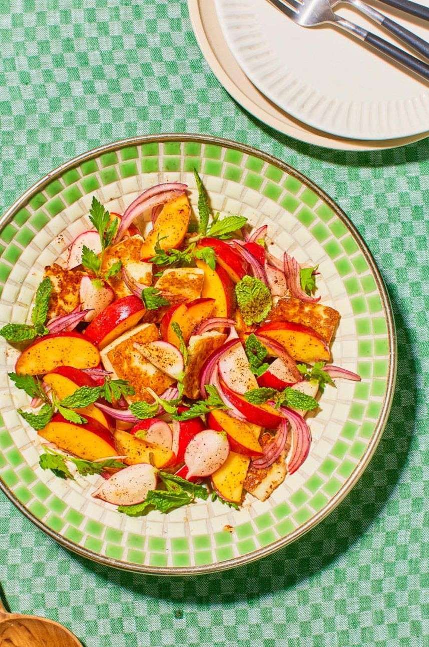 Overhead shot of peach and halloumi salad with mint and red onion on a decorative plate, atop a green checkered tablecloth.