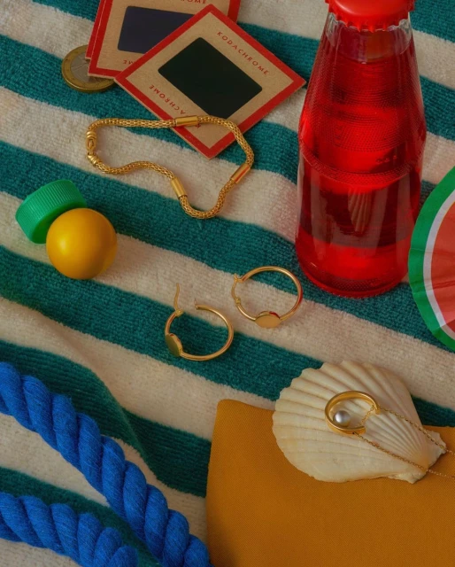 Still life of jewelry, a beverage bottle, and film slides on a striped beach towel with bright summer colors and a playful mood.