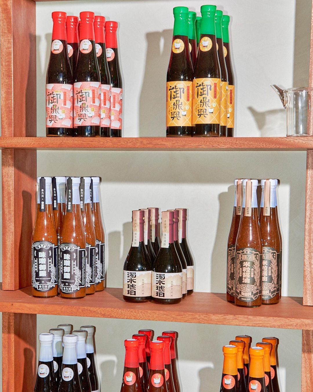 Bottles of sauce are displayed on a wooden shelf against a white background; food and beverage presentation with colorful labels.