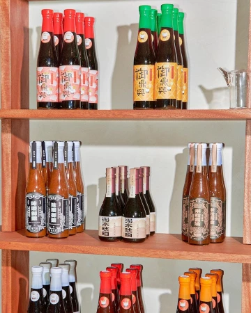 Bottles of sauce are displayed on a wooden shelf against a white background; food and beverage presentation with colorful labels.