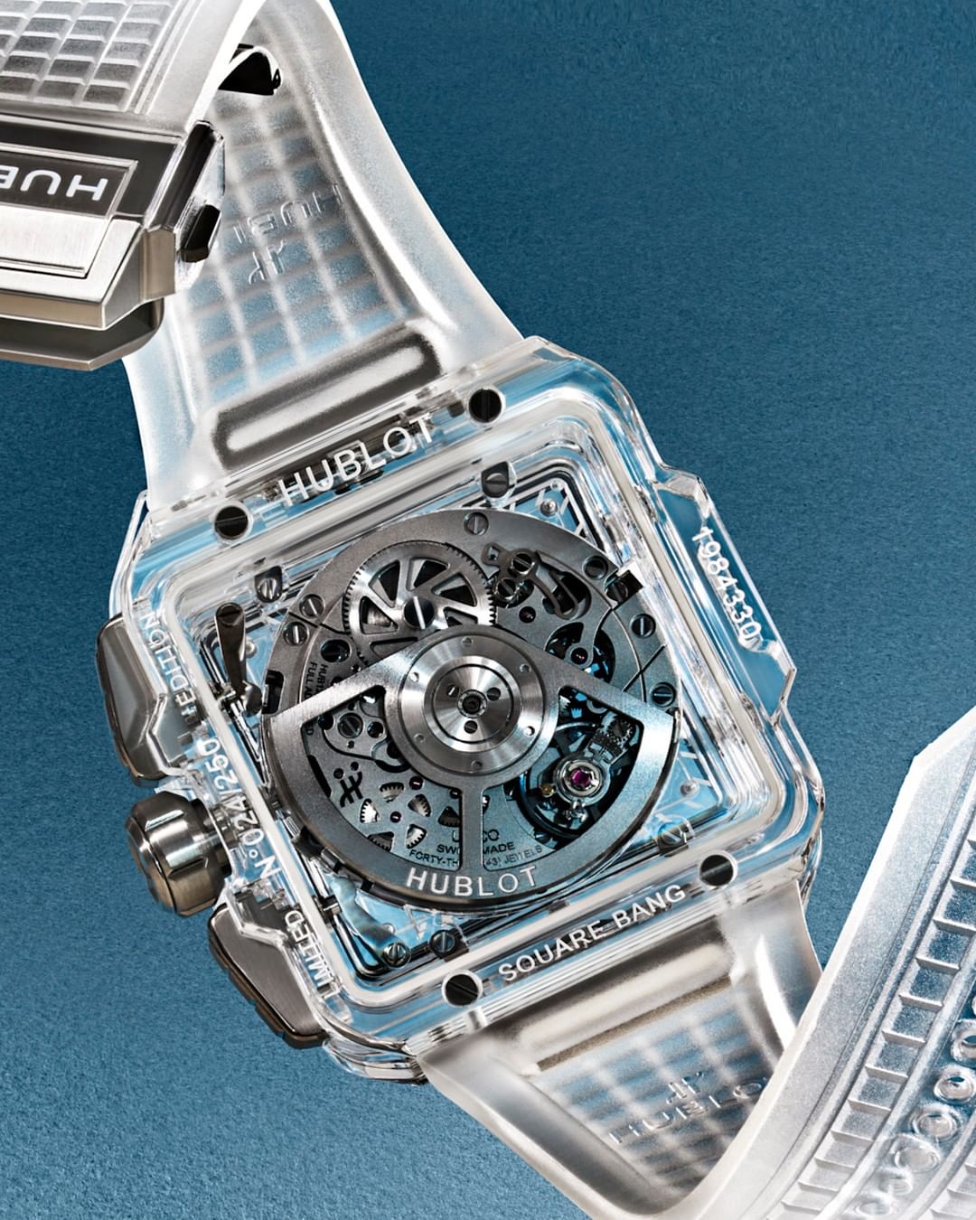 Hublot Square Bang watch close-up featuring a transparent case, intricate inner mechanisms, and a modern design against a blue backdrop.