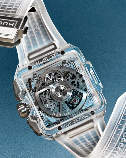 Hublot Square Bang watch close-up featuring a transparent case, intricate inner mechanisms, and a modern design against a blue backdrop.