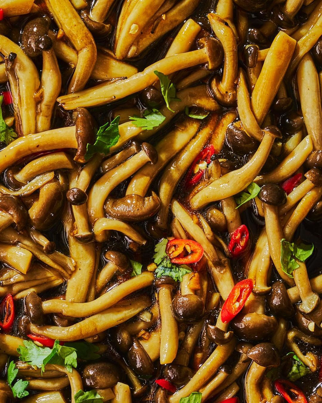 Overhead shot of stir-fried shimeji mushrooms with soy sauce, red chili peppers, and parsley. Close-up of the Asian-inspired dish.