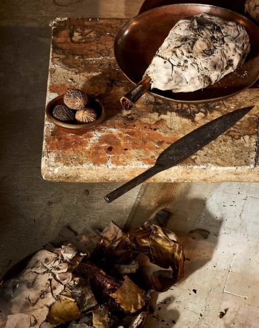 Overhead shot of a food dish with nuts, a knife, and peeling on a textured wooden table with a worn, aged appearance.