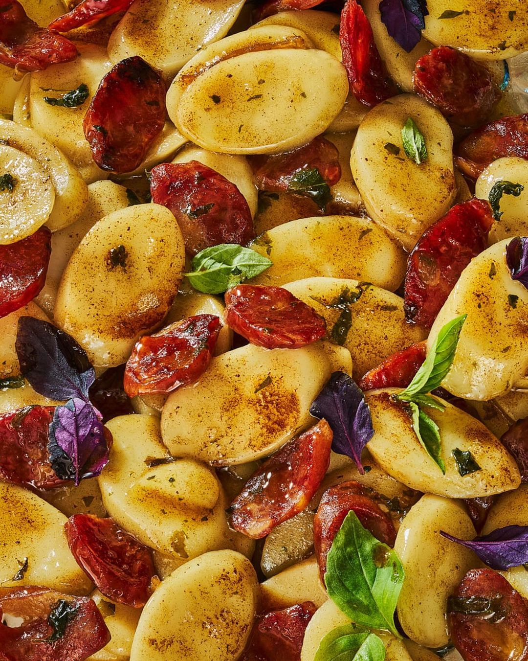 Overhead shot of golden gnocchi with charred chorizo slices and green and purple basil leaves, offering a visually appealing food composition.