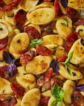 Overhead shot of golden gnocchi with charred chorizo slices and green and purple basil leaves, offering a visually appealing food composition.