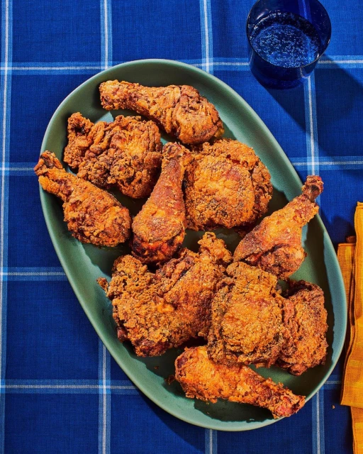 Overhead shot of fried chicken pieces on a green platter, set on a blue plaid tablecloth with a glass of water and yellow napkin.