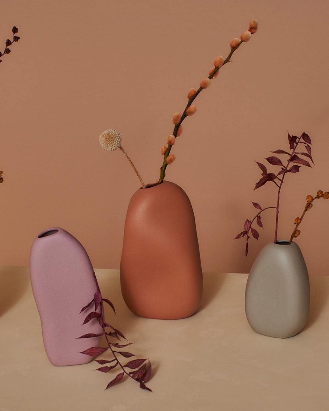 Still life arrangement features several ceramic vases in varying shapes and colors, each holding different types of dried floral stems.