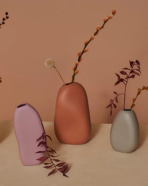 Still life arrangement features several ceramic vases in varying shapes and colors, each holding different types of dried floral stems.