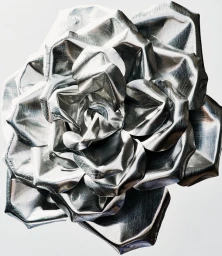 Close-up macro shot of a sculptural metallic silver flower crafted from crinkled foil against a clean white background.