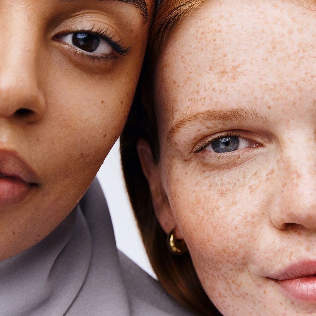 Close-up studio shot of two women with different skin tones, one with freckles, fair complexion, and red hair, showcasing skin diversity.