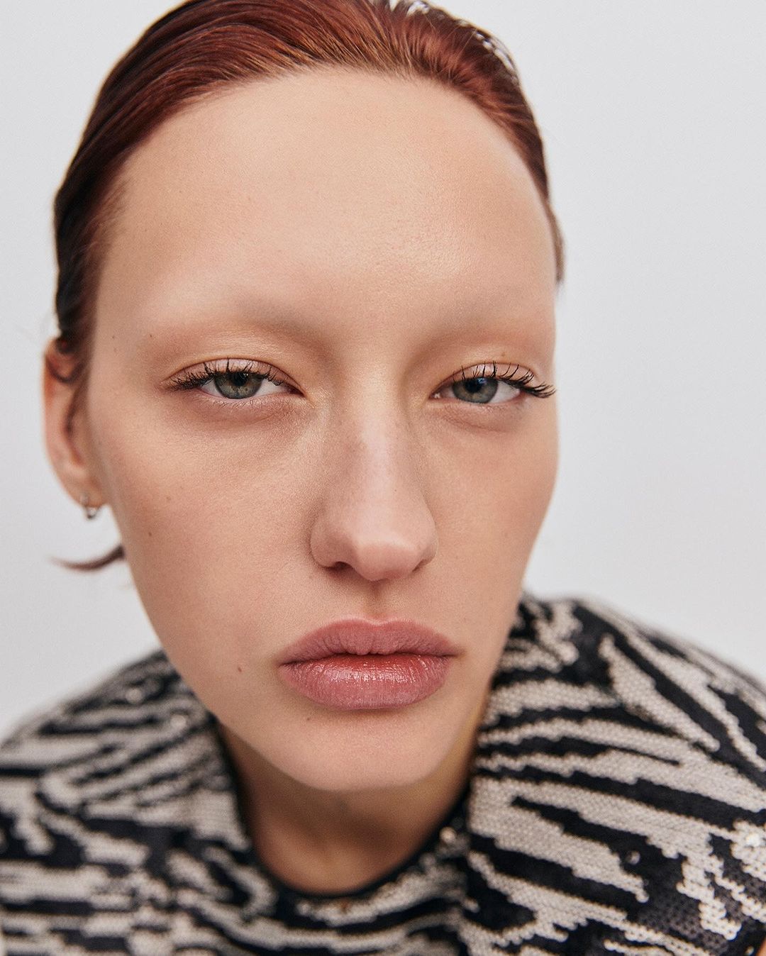 Close-up portrait of a redhead woman with light skin in a zebra-striped sweater, shot in a photo studio with diffused lighting.