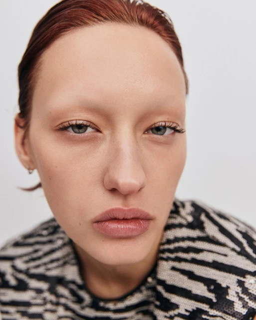 Close-up portrait of a redhead woman with light skin in a zebra-striped sweater, shot in a photo studio with diffused lighting.