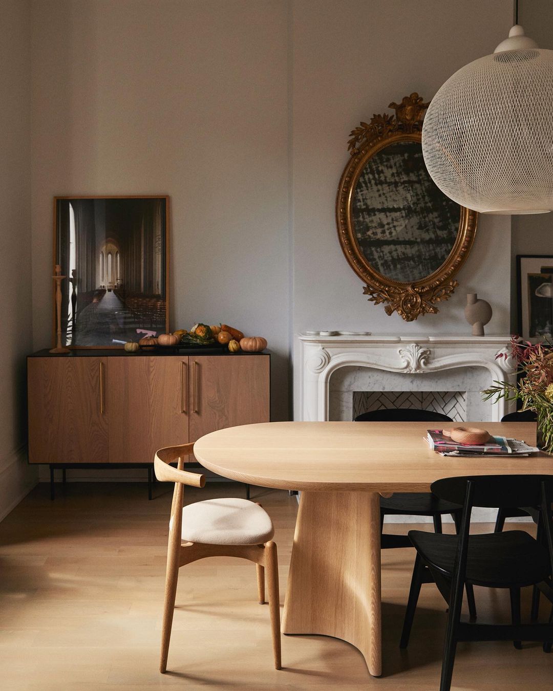Interior view of a dining room with a wood table surrounded by chairs, a sideboard with gourds, and a decorative mantelpiece.