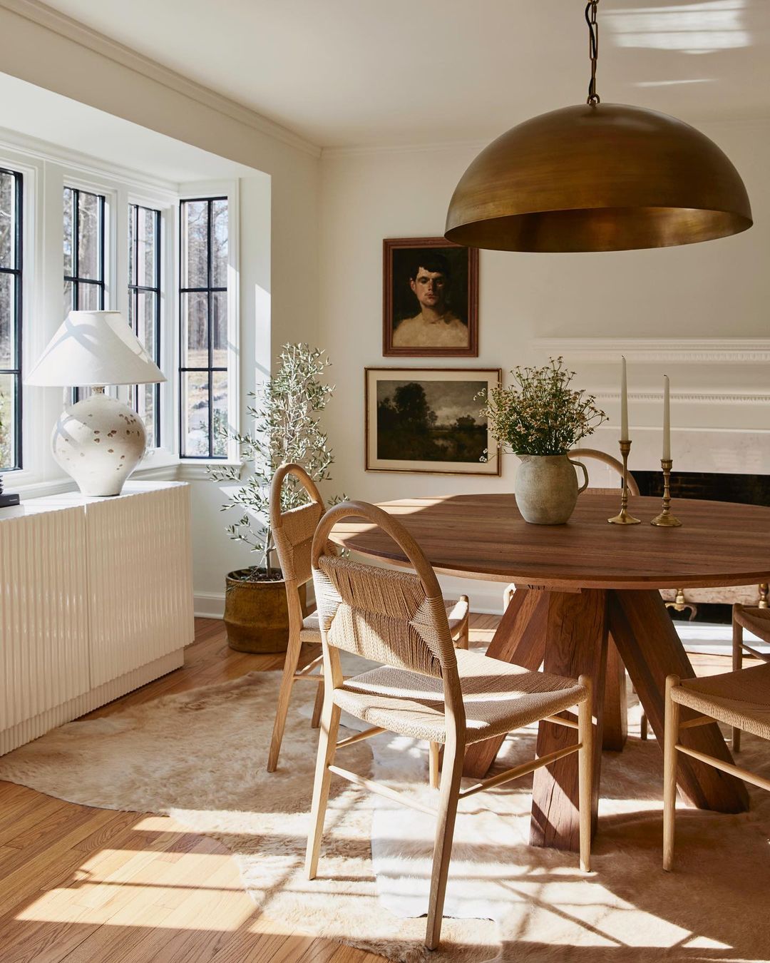 Dining room interior featuring a round wooden table, woven chairs, and a pendant light fixture, creating a warm, inviting atmosphere.