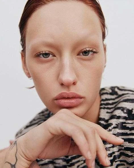 Close-up portrait of a woman with fair skin, light red hair, and light makeup wearing a black and white patterned top.