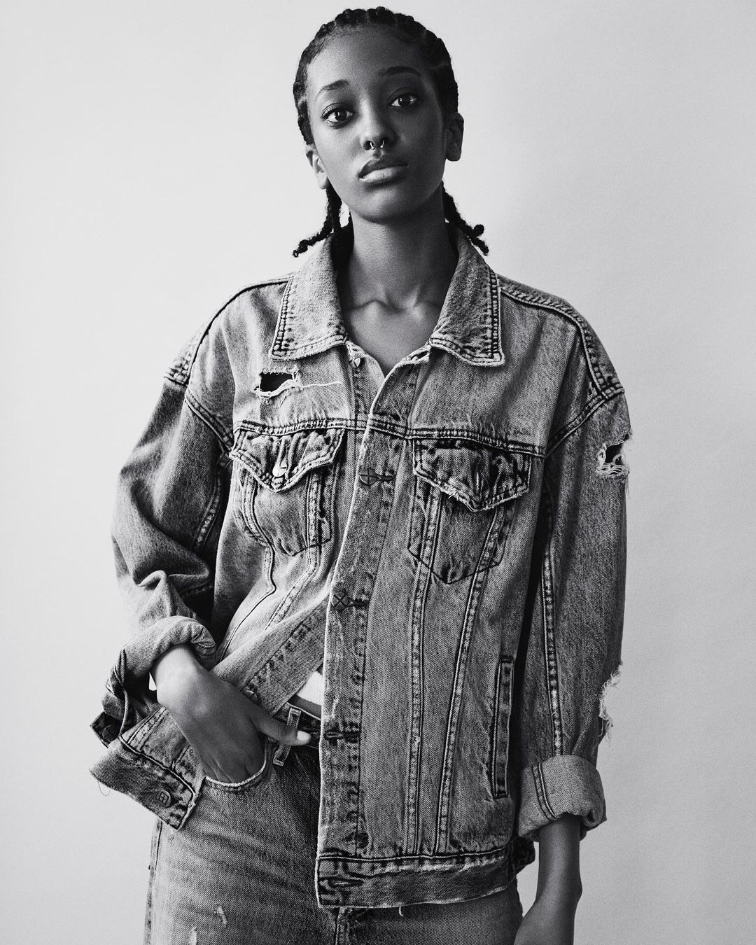 Portrait of an African American female wearing a distressed denim jacket and jeans against a plain background in black and white.