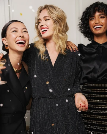 Three smiling multi-ethnic women in festive dresses celebrate with confetti.  Indoor party or fashion editorial concept.
