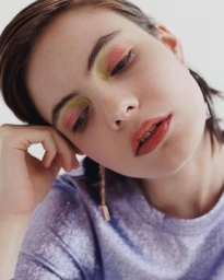 Close-up portrait of a young woman with colourful eyeshadow and a purple textured top, photographed by Heather Moore.