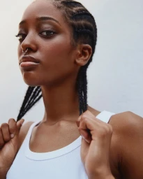 Close-up portrait of a Black woman with braided hair and a septum ring wearing a white tank top, photographed by Heather Moore.