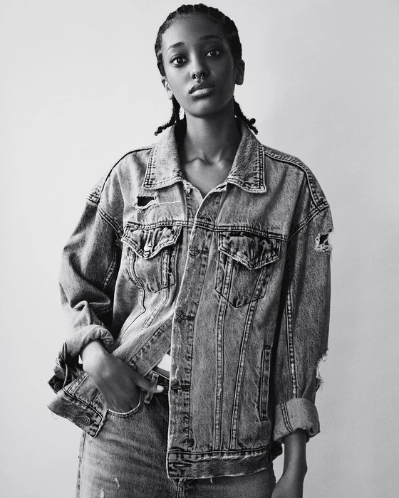 Black and white portrait of a young woman wearing a distressed denim jacket against a plain background