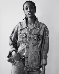 Black and white portrait of a young woman wearing a distressed denim jacket against a plain background
