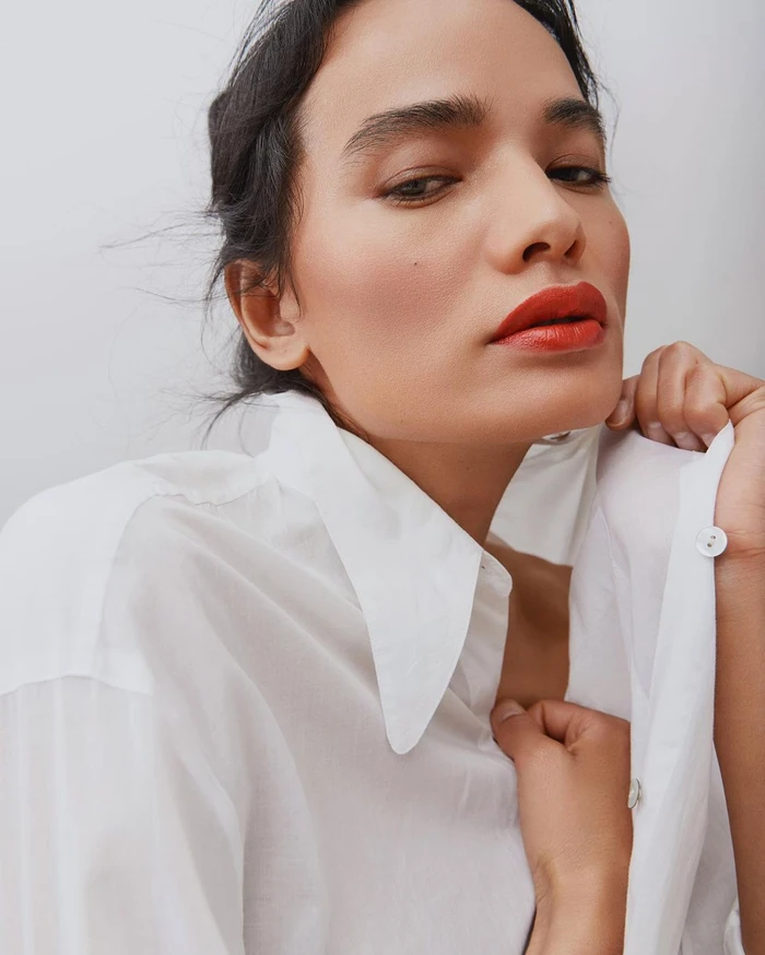 Close up portrait of a woman with bold red lipstick wearing a crisp white button up shirt against a plain light background