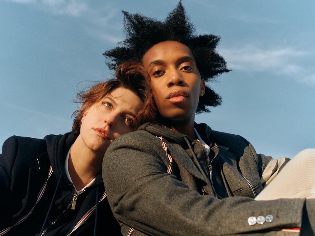 Two people posing close together outdoors against a clear blue sky, photographed by Heather Sten in New York.