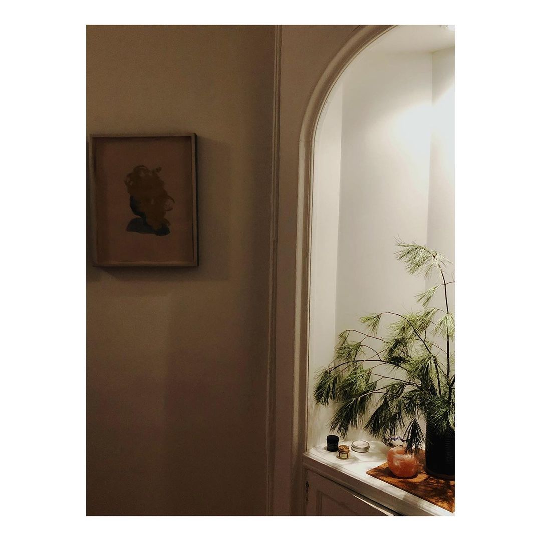 Interior scene with framed art hanging on a wall, a decorative alcove with a plant, candle holders, and warm lighting in a home.
