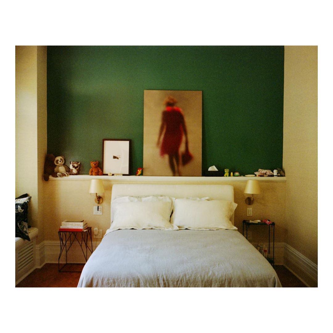 Bedroom with a bed, a framed print of a woman in a red dress, stuffed animals and decorative objects, set against a green wall.