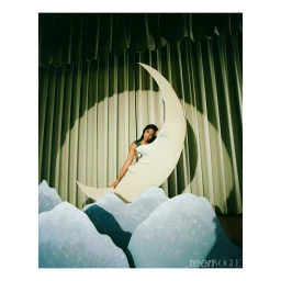 Woman posing behind a large crescent moon prop in front of green curtains and pale blue mountain cutouts by Heather Sten