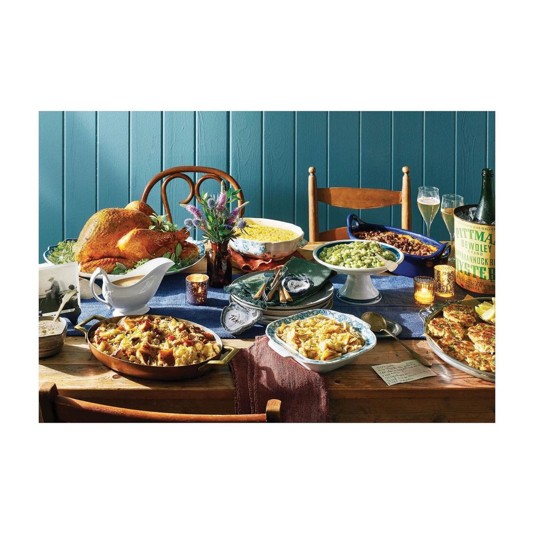 Thanksgiving dinner spread on a table featuring roast turkey, various casseroles, champagne flutes, and a rustic wood background.