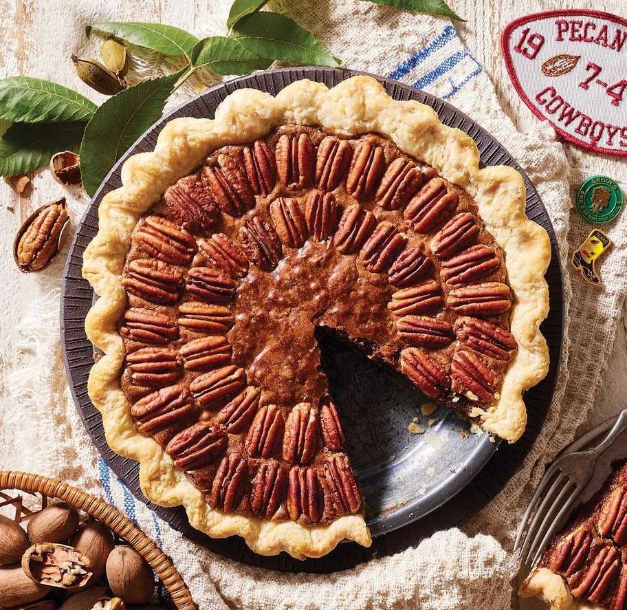 Overhead shot of a pecan pie with a slice removed, showcasing the nut arrangement, golden-brown filling, and flaky crust.