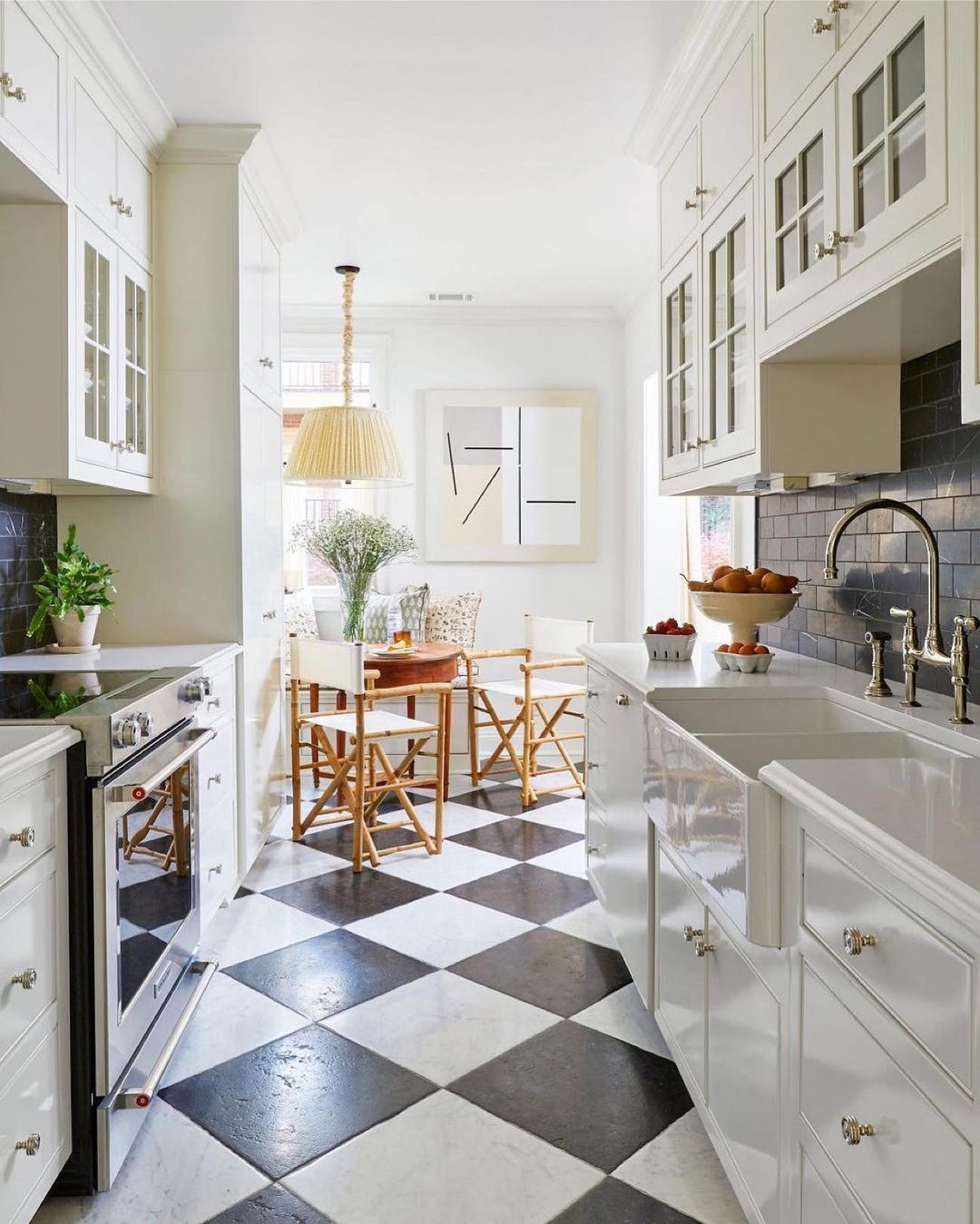 Bright, modern kitchen interior with white cabinets, black and white checkered floor, dining table set with chairs, and neutral pendant light.