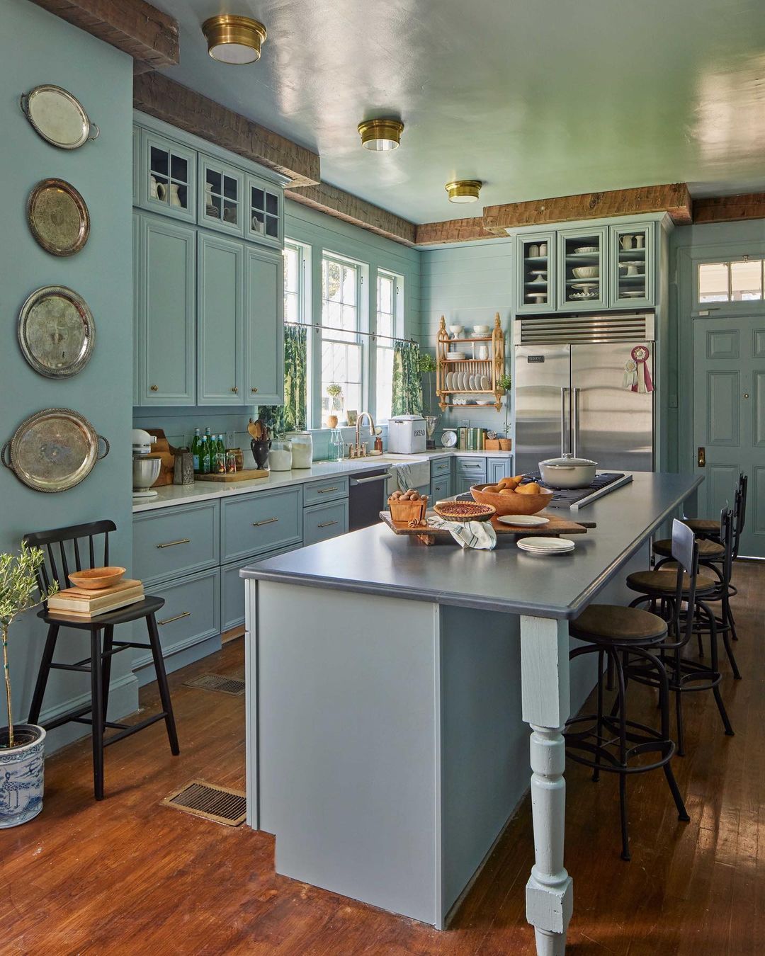 A spacious light-blue kitchen features a large center island with seating, wooden floors, natural lighting, and classic appliances.