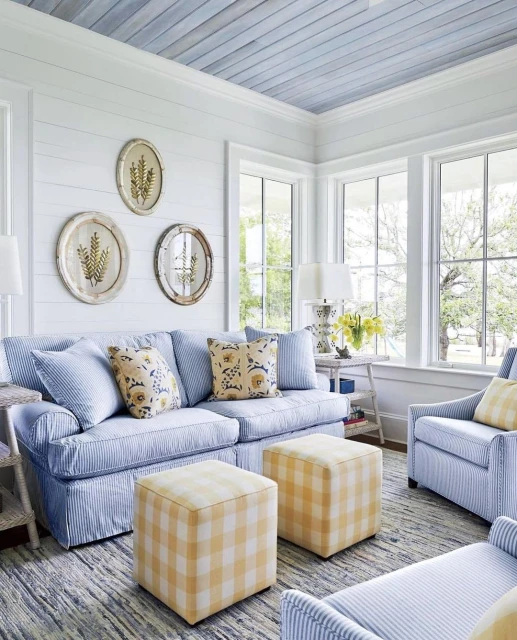 Living room interior featuring a blue and white striped sofa, yellow and white plaid ottomans, armchairs, and natural light from large windows.