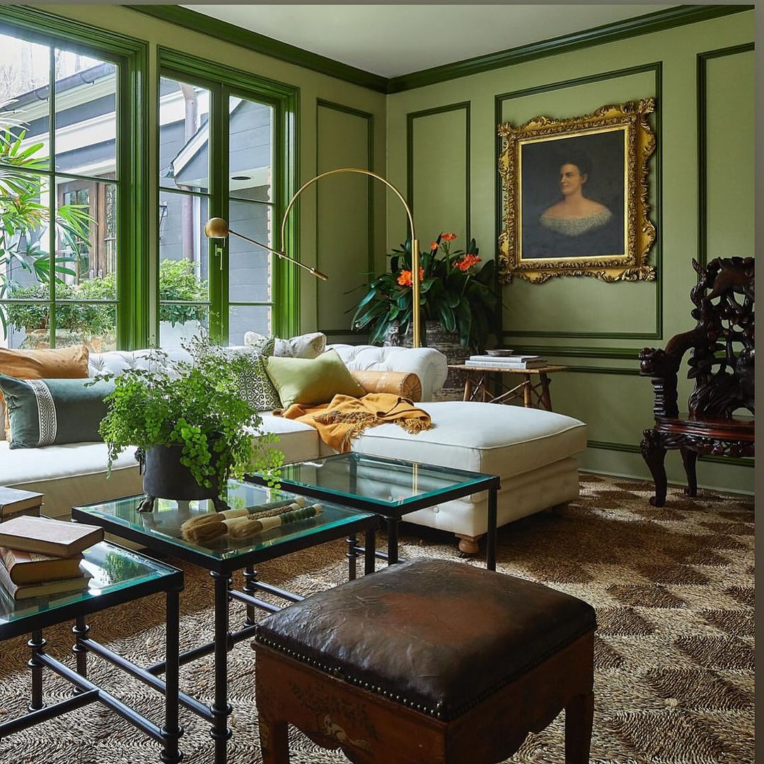 Living room interior with green walls, large windows, white couch, and glass coffee tables. Portrait painting visible on the wall.