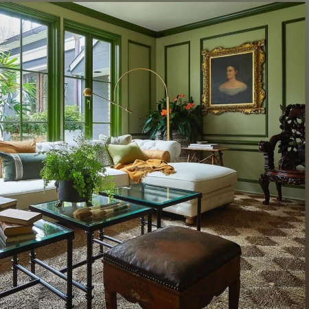 Living room interior with green walls, large windows, white couch, and glass coffee tables. Portrait painting visible on the wall.