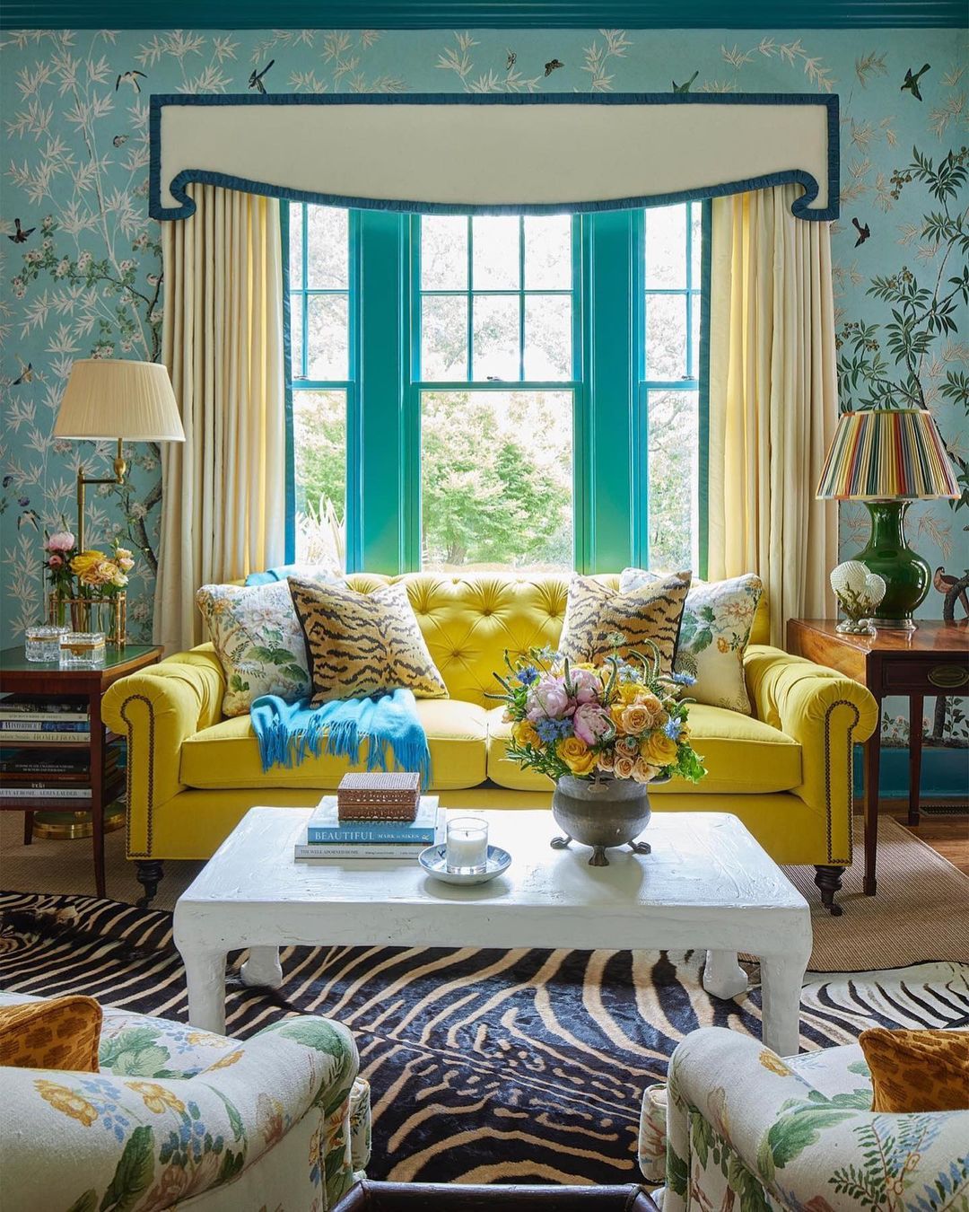 Bright and colorful interior design featuring a yellow sofa, floral armchairs, and a striking zebra-print rug, illuminated by natural light.